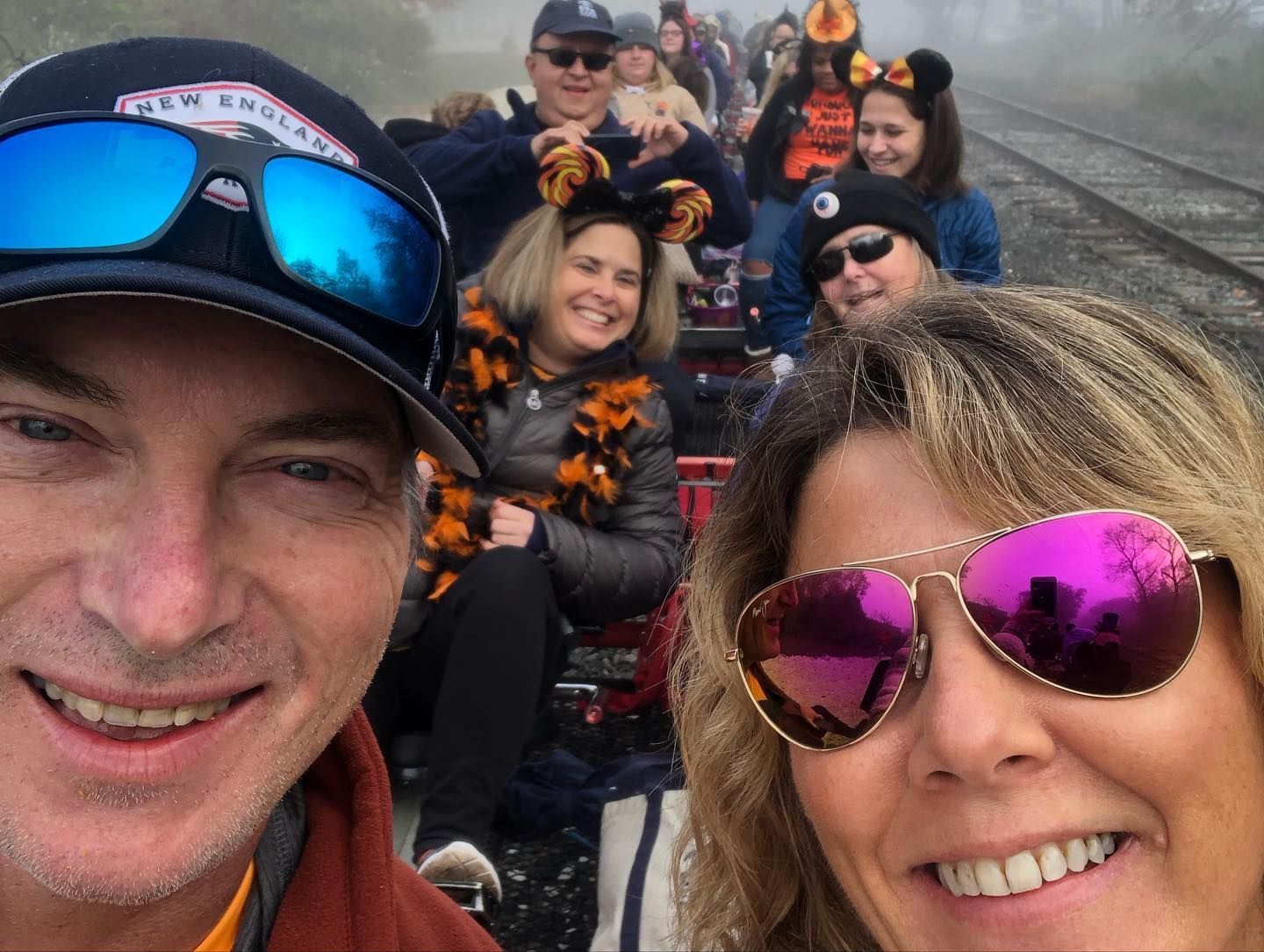 Group selfie of people sitting on a railway track, smiling and wearing sunglasses and winter hats