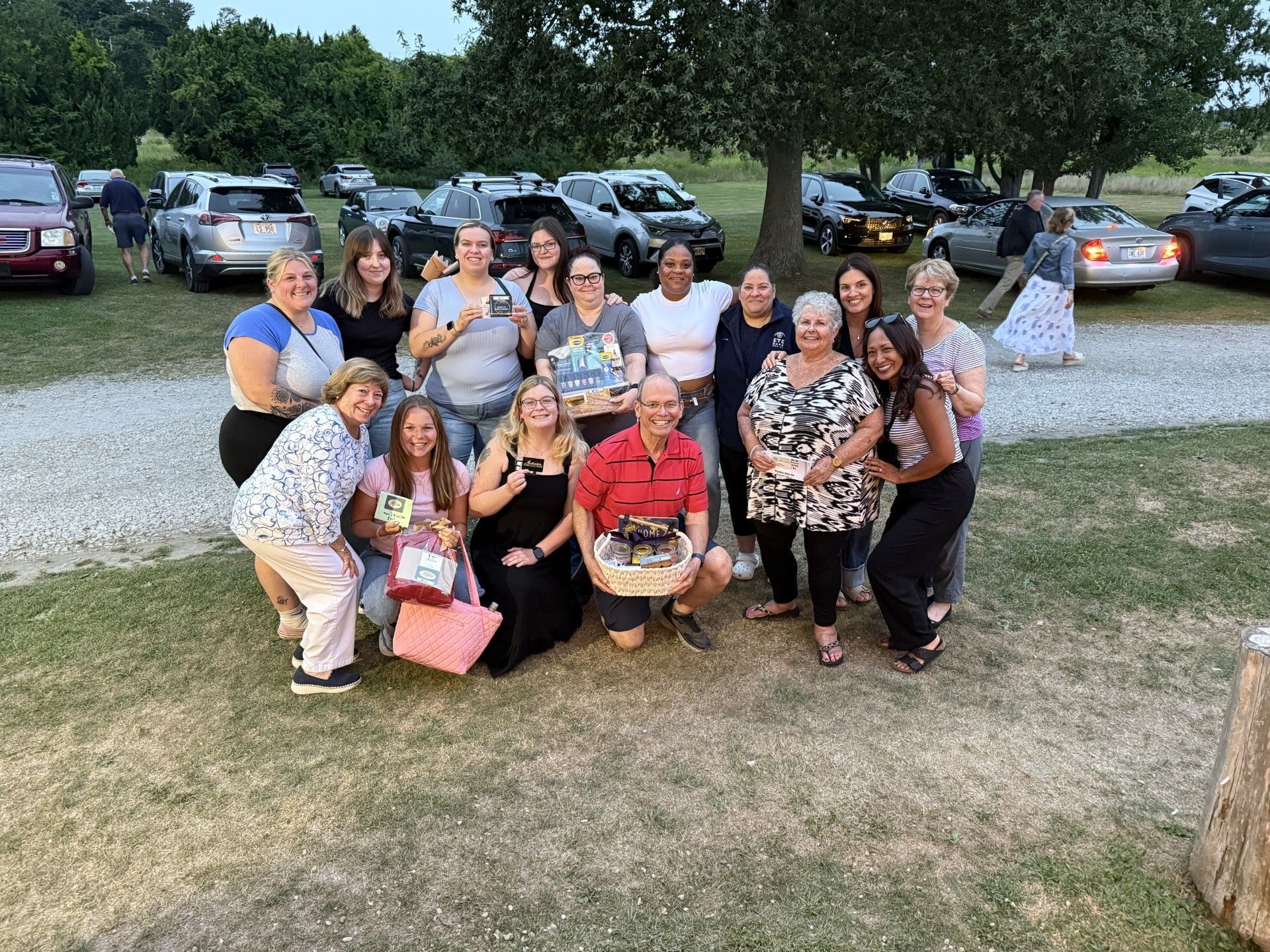 Group of people posing together outdoors near parked cars, smiling for a casual gathering.
