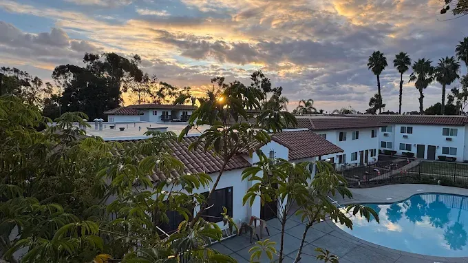 Resort pool and white buildings at sunset with palm trees and cloudy sky