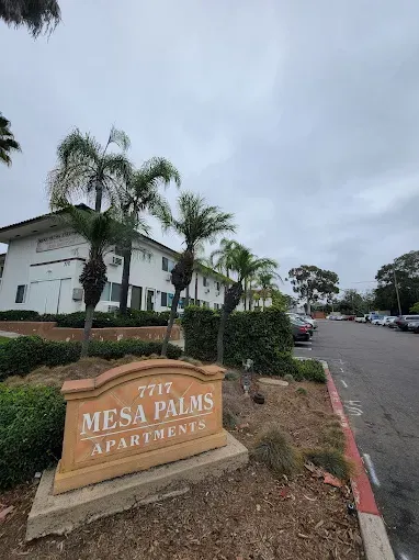 Mesa Palms Apartments sign by palm trees along a street on a cloudy day