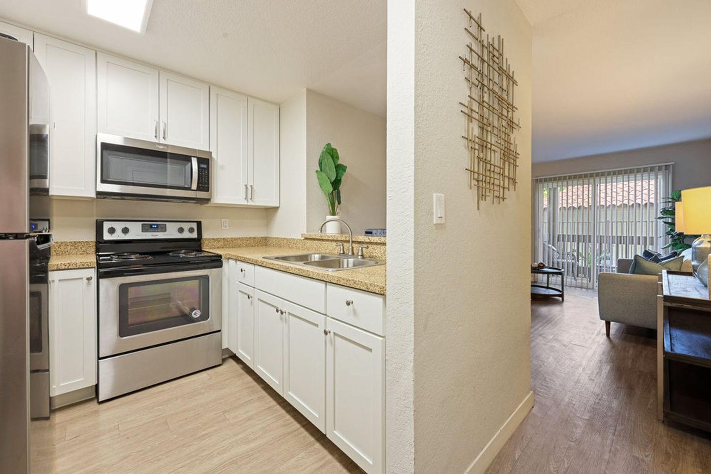 Bright kitchen with white cabinets and stainless-steel appliances, opening to a living room with sliding glass doors.