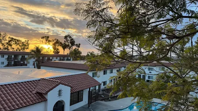Sunset over white residential buildings with red-tiled roofs and trees in the foreground