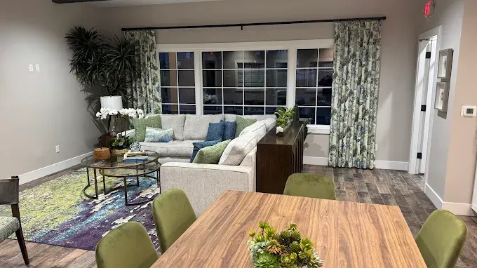 Modern lounge with sofas, green chairs, wooden tables, and large windows in a bright common area