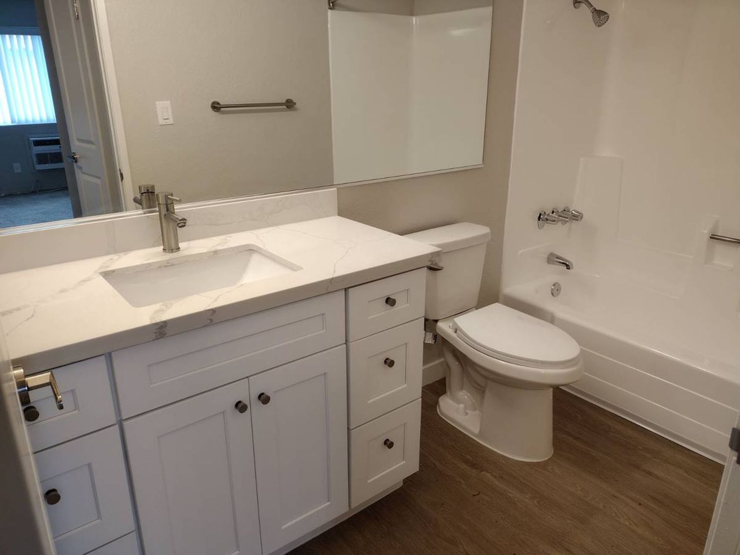 Accessible bathroom with white vanity, sink, toilet, and tub with grab bars and wood-look floor.