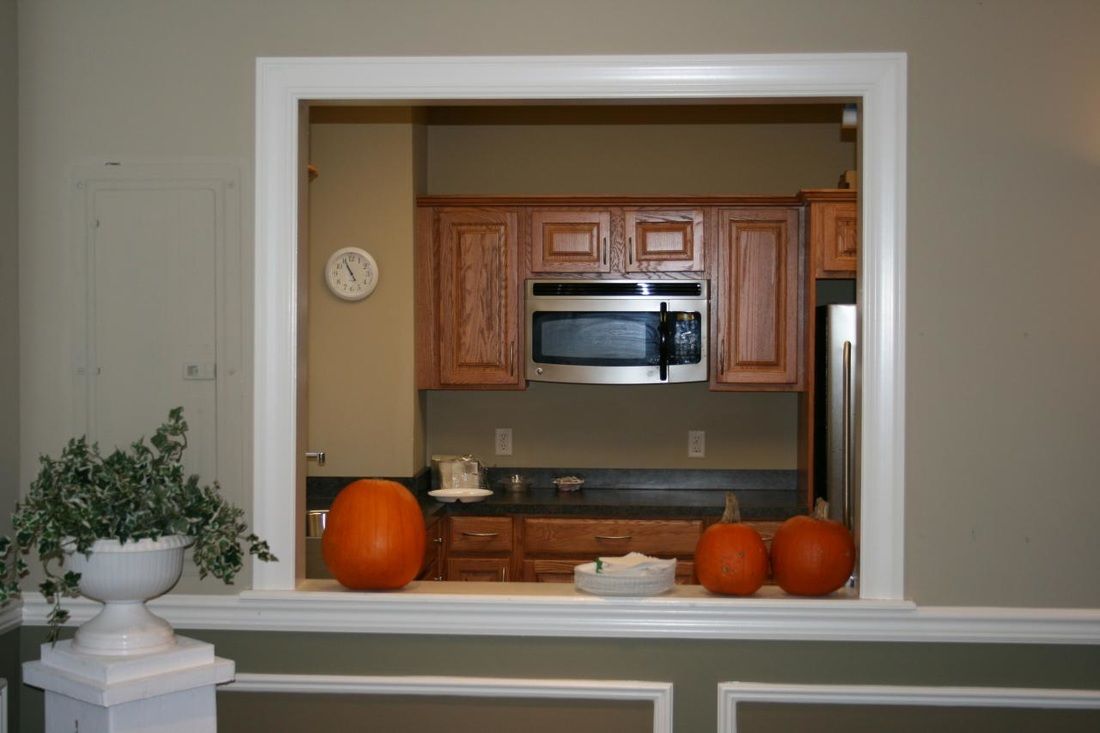 A view of a kitchen through a window with pumpkins on the counter