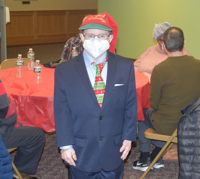 A man wearing a mask and a santa hat stands in front of a table
