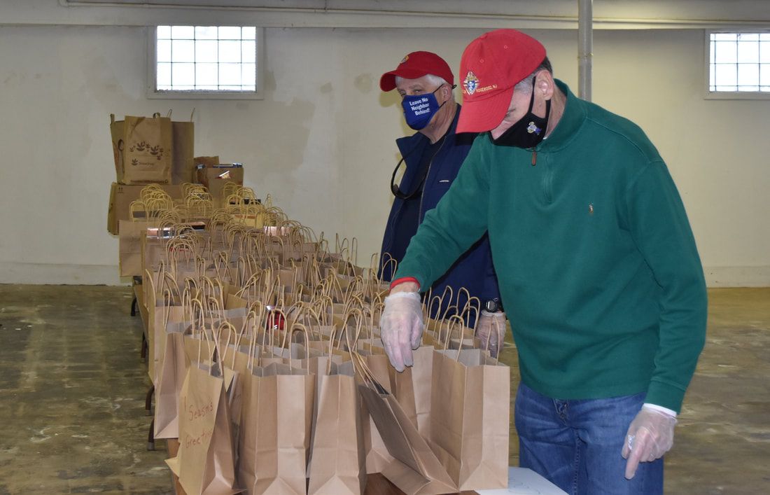 Two men wearing face masks are standing in front of a row of brown bags.
