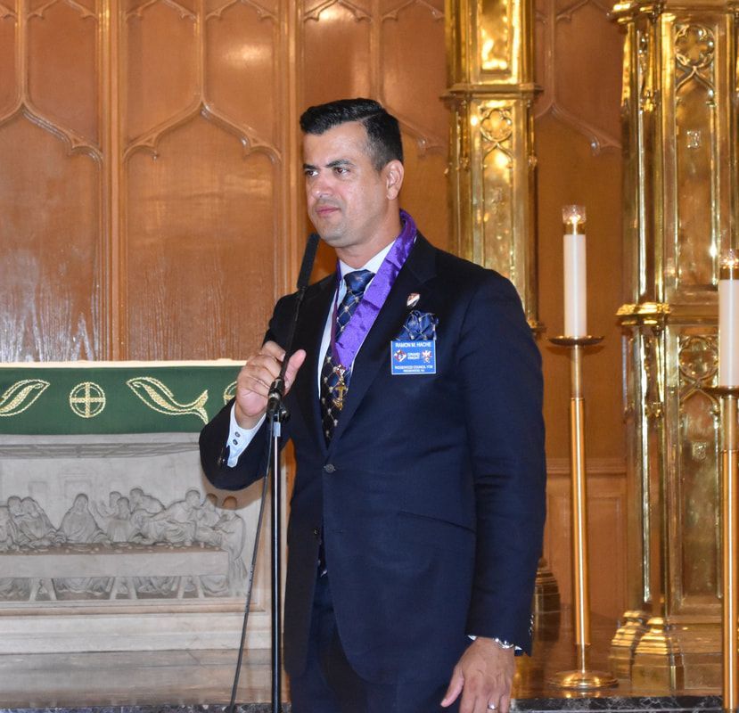 A man in a suit and tie is speaking into a microphone