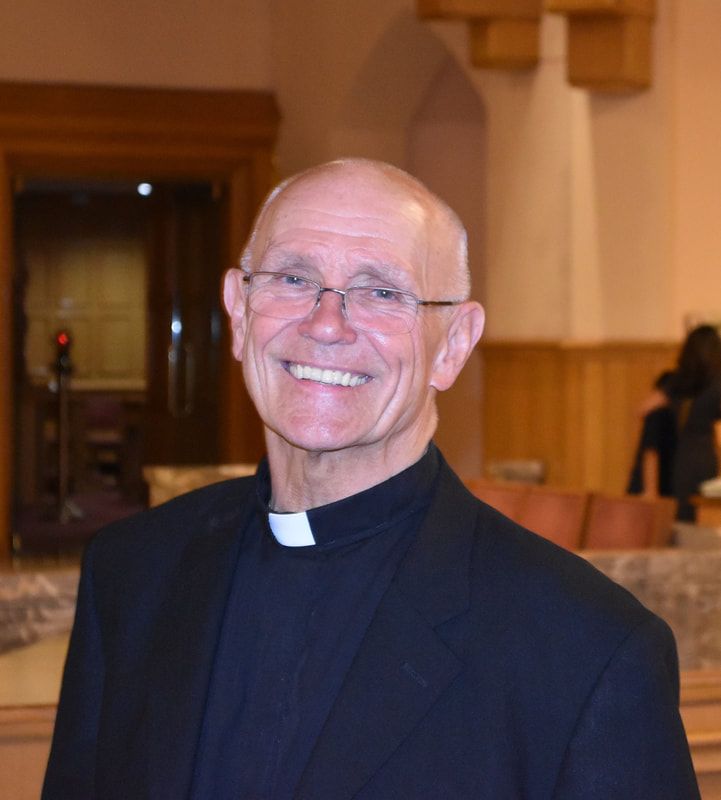 A man in a black suit and white collar is smiling