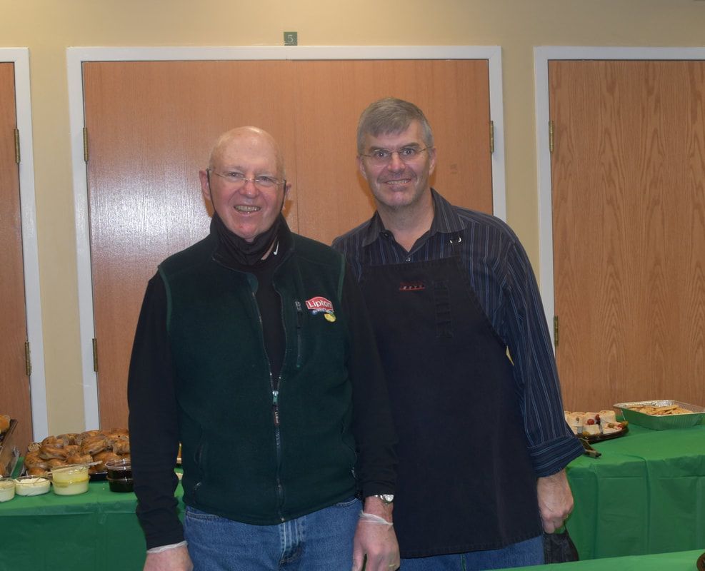 Two men standing next to each other in front of a table with food on it