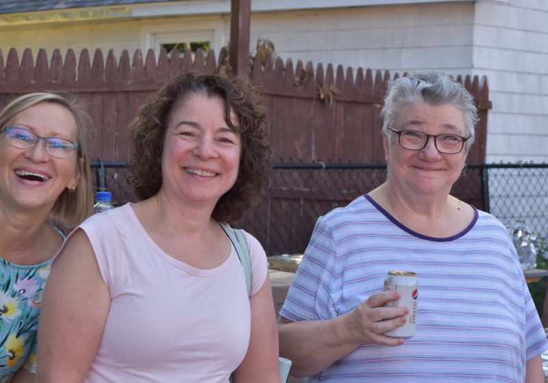 Three women are posing for a picture in front of a wooden fence.
