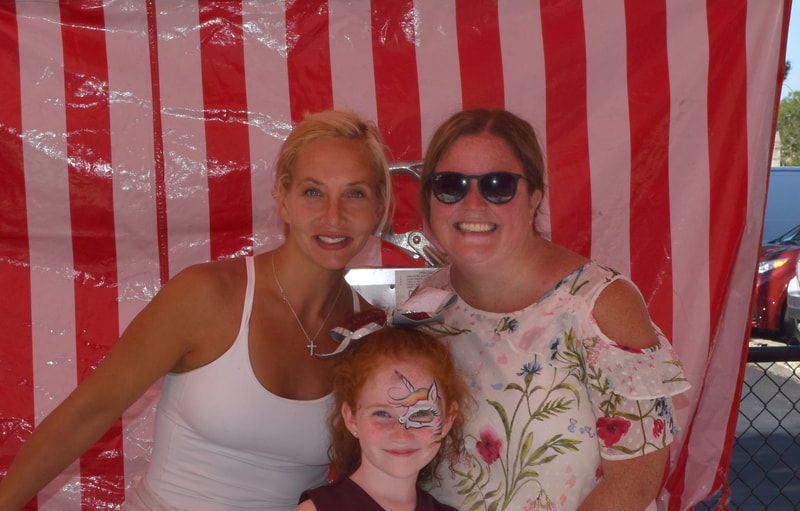 Two women and a little girl are posing for a picture in front of a red and white striped tent.