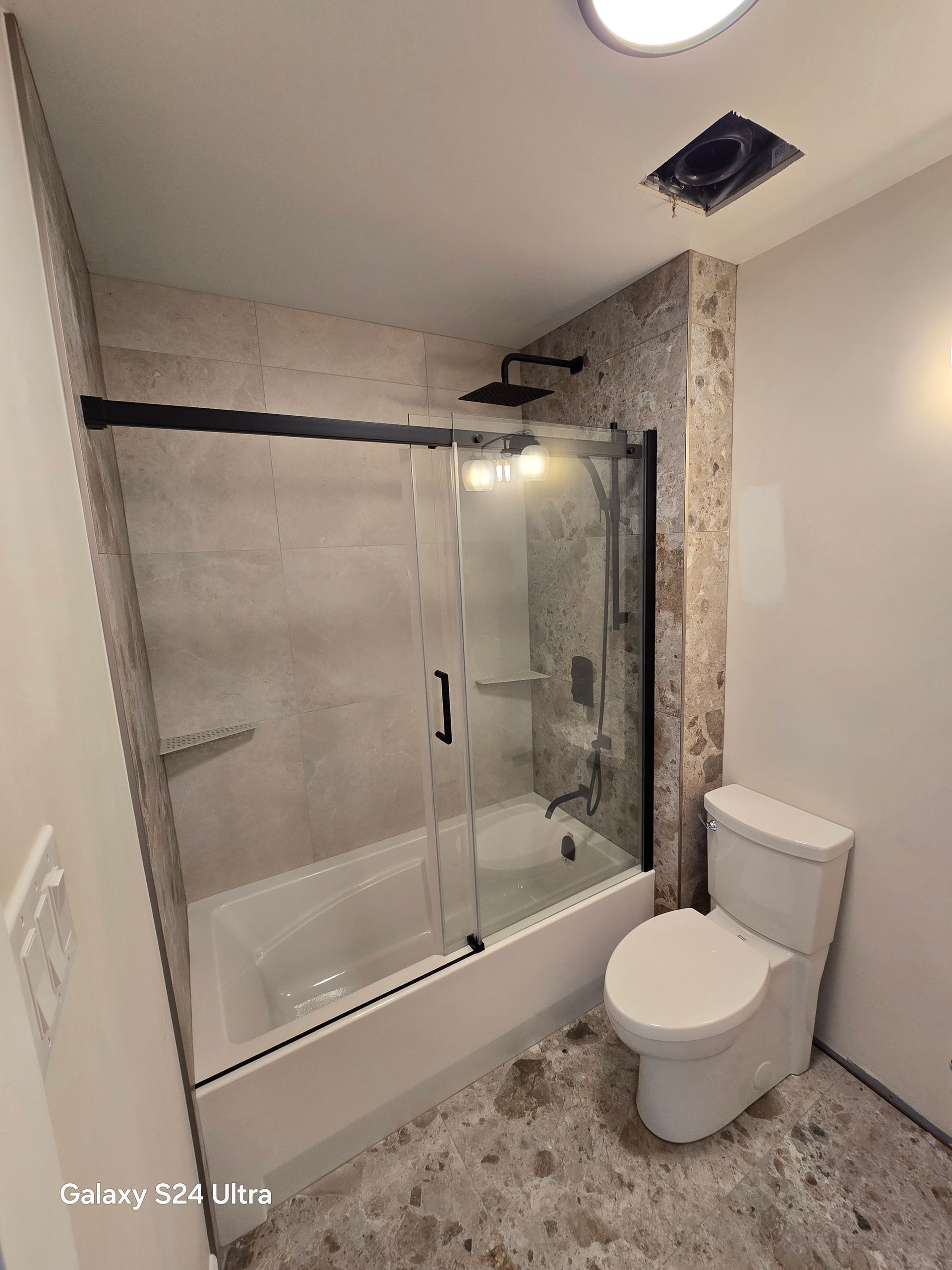 Salle de bains avec douche à l'italienne en verre, toilettes et murs et sol carrelés à motifs mouchetés