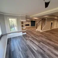 A wide view of a modern room with wood-look flooring, a fireplace, and a staircase leading to an upper level.