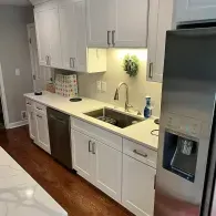 A modern white kitchen featuring light-colored cabinets, a stainless steel dishwasher, a sink, and a refrigerator.