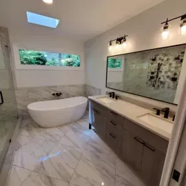 Modern bathroom with a freestanding white tub, double vanity with dark cabinets, marble tile, and a large wall mirror.