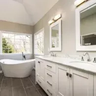 A bright bathroom featuring a white freestanding tub, a long double vanity with white cabinets, and large mirrors.