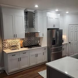 A bright, modern kitchen featuring white cabinets, stainless steel appliances, and a bold patterned tile backsplash.