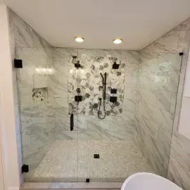 A walk-in shower with marble-look tile, a floral accent wall, a pebble floor, and glass walls with black hardware.