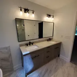 A modern bathroom vanity with a double sink, dark cabinets, a long rectangular mirror, and two stylish light fixtures.