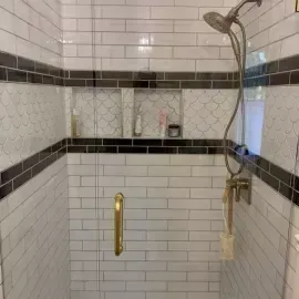 A tiled shower with white subway tiles, a black accent stripe, two wall niches, and a gold-toned shower head and door handle.