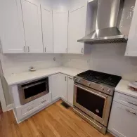 A modern kitchen with white cabinets, a stainless steel stove with a matching range hood, and a built-in microwave.