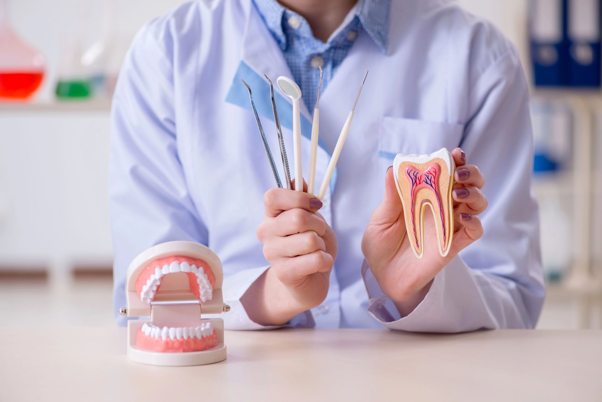 Dentista con camice che tiene in mano strumenti odontoiatrici e un modello di dente in uno studio dentistico