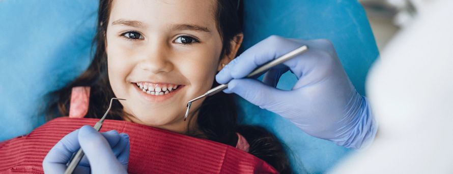 Dentista che visita un bambino sorridente con uno specchietto dentale e un aspiratore