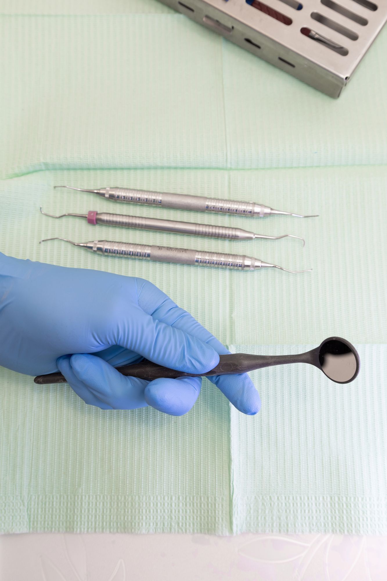 Mano guantata che tiene uno specchietto dentale sopra strumenti odontoiatrici disposti su un telo verde sterile