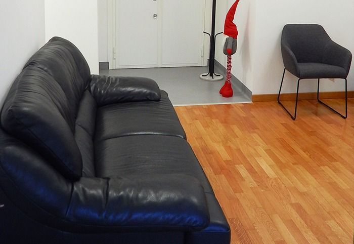 Soggiorno con divano in pelle nera, poltrona grigia, pavimento in legno e statuina decorativa rossa vicino alla porta