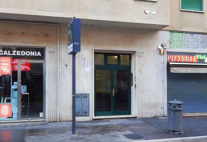 Vetrina a livello della strada con una porta dalla cornice verde tra un negozio Calzedonia e una pizzeria.
