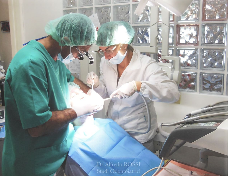 Dentisti con mascherine e divise verdi curano un paziente in uno studio dentistico luminoso.