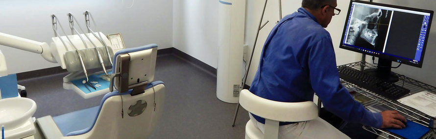 Tecnico in camice blu esamina radiografie dentali su due monitor in una sala clinica