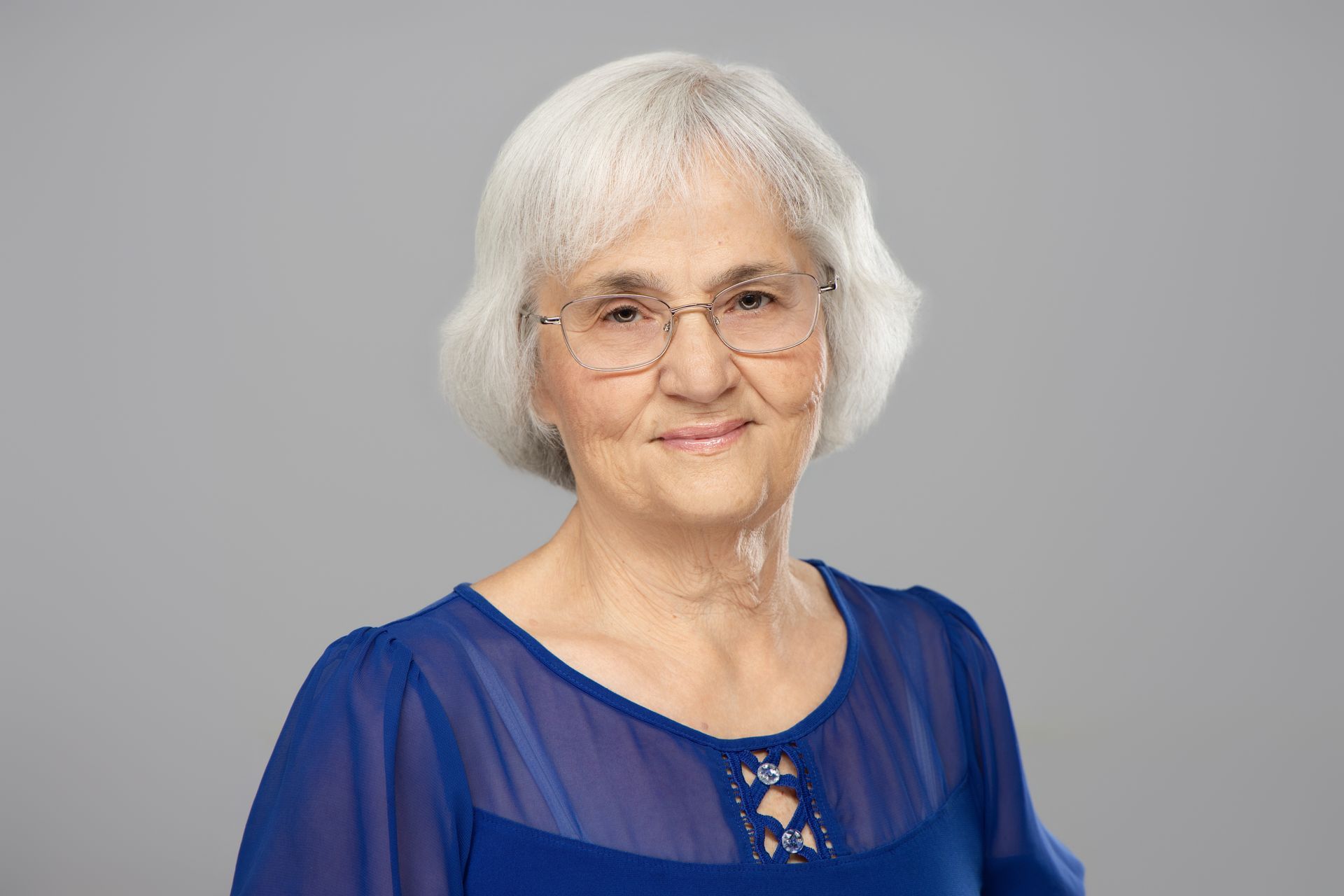 Smiling woman with short white hair wearing a blue blouse against a gray background