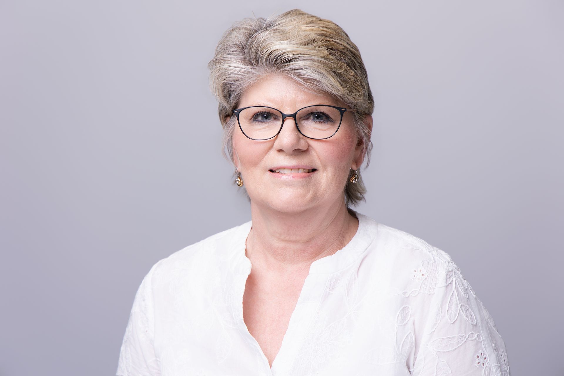 Smiling woman in glasses wearing a white blouse against a light gray background