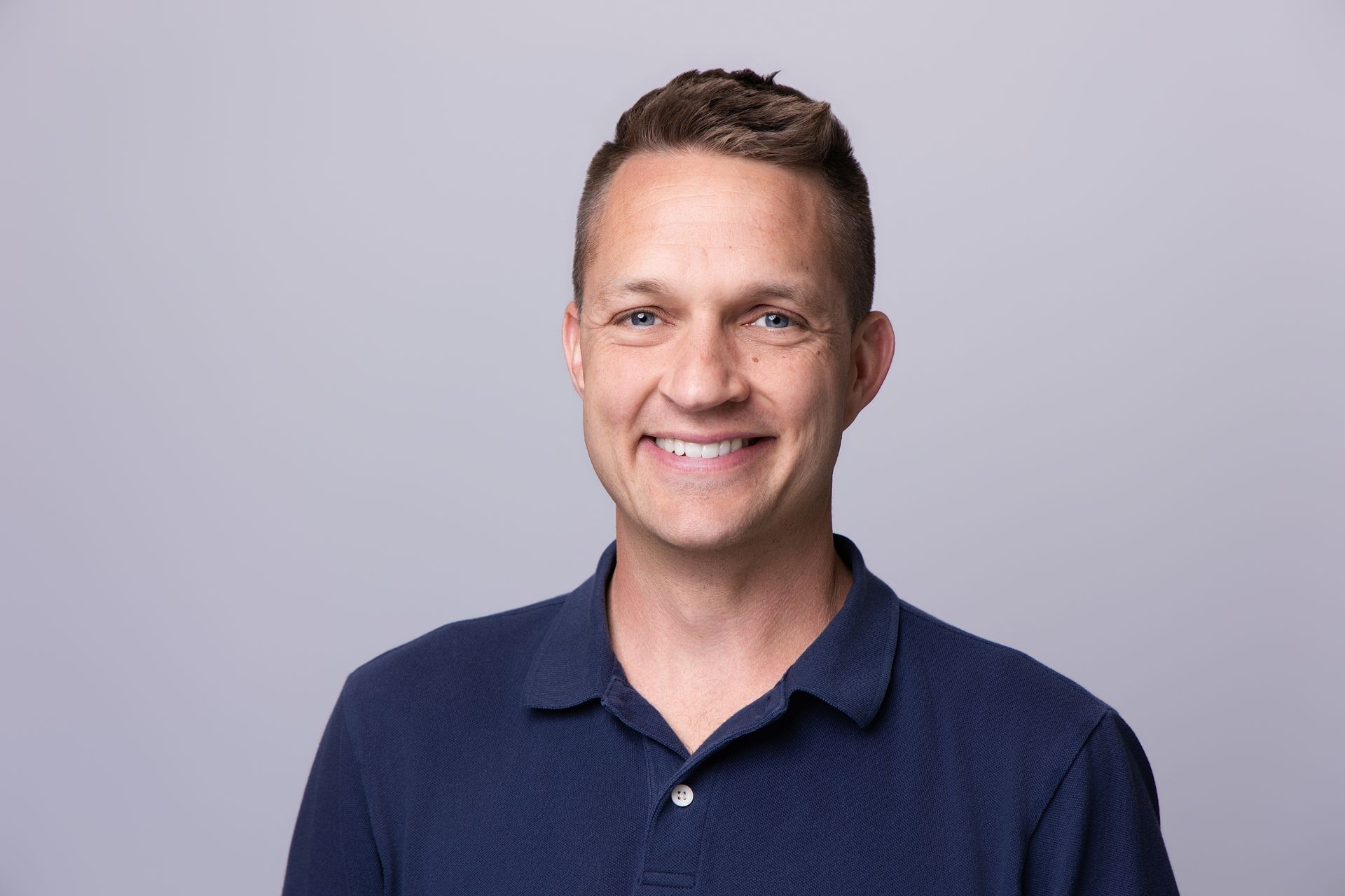 Smiling man in a navy polo shirt against a light gray background