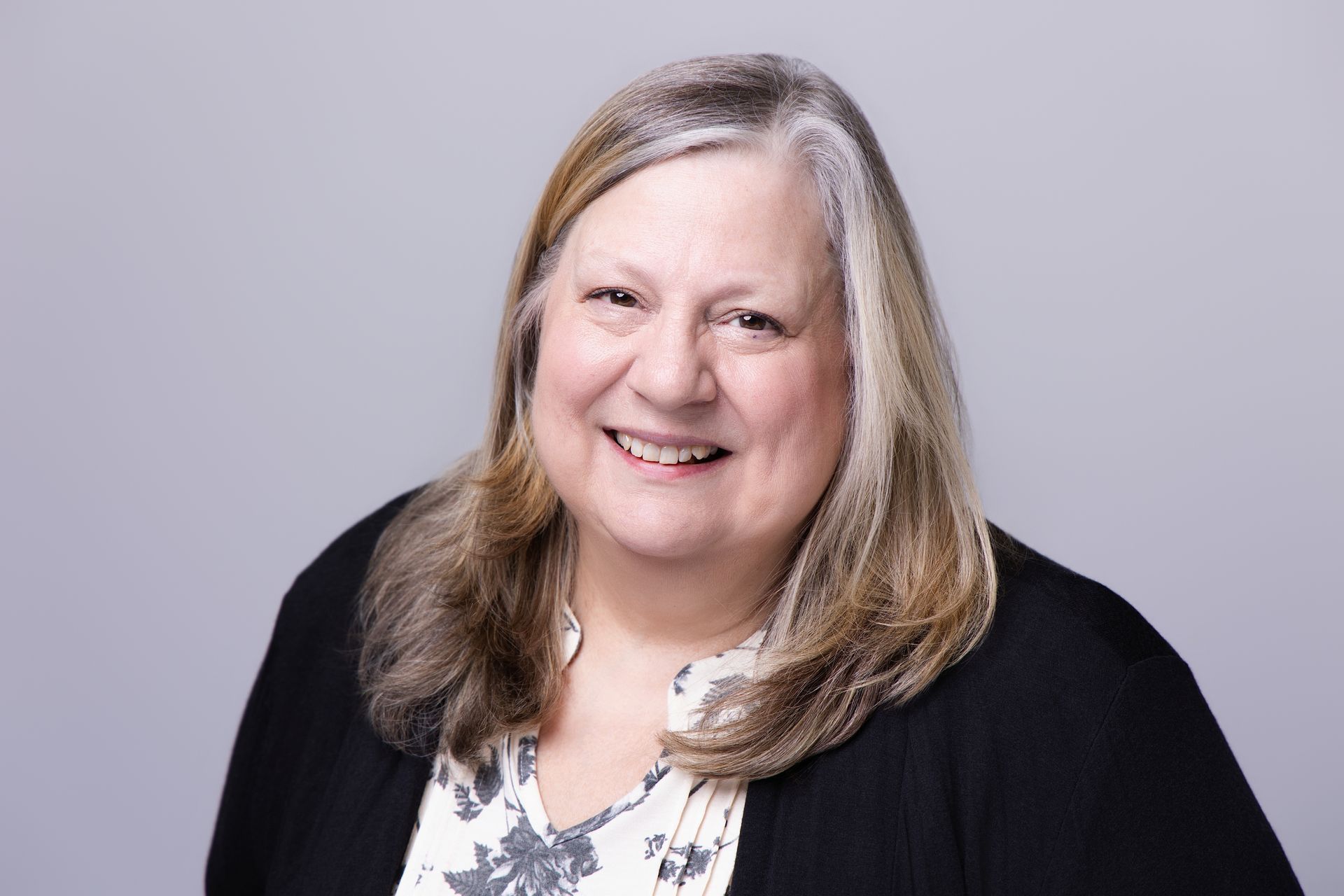 Smiling woman in a black cardigan and floral top against a light gray background
