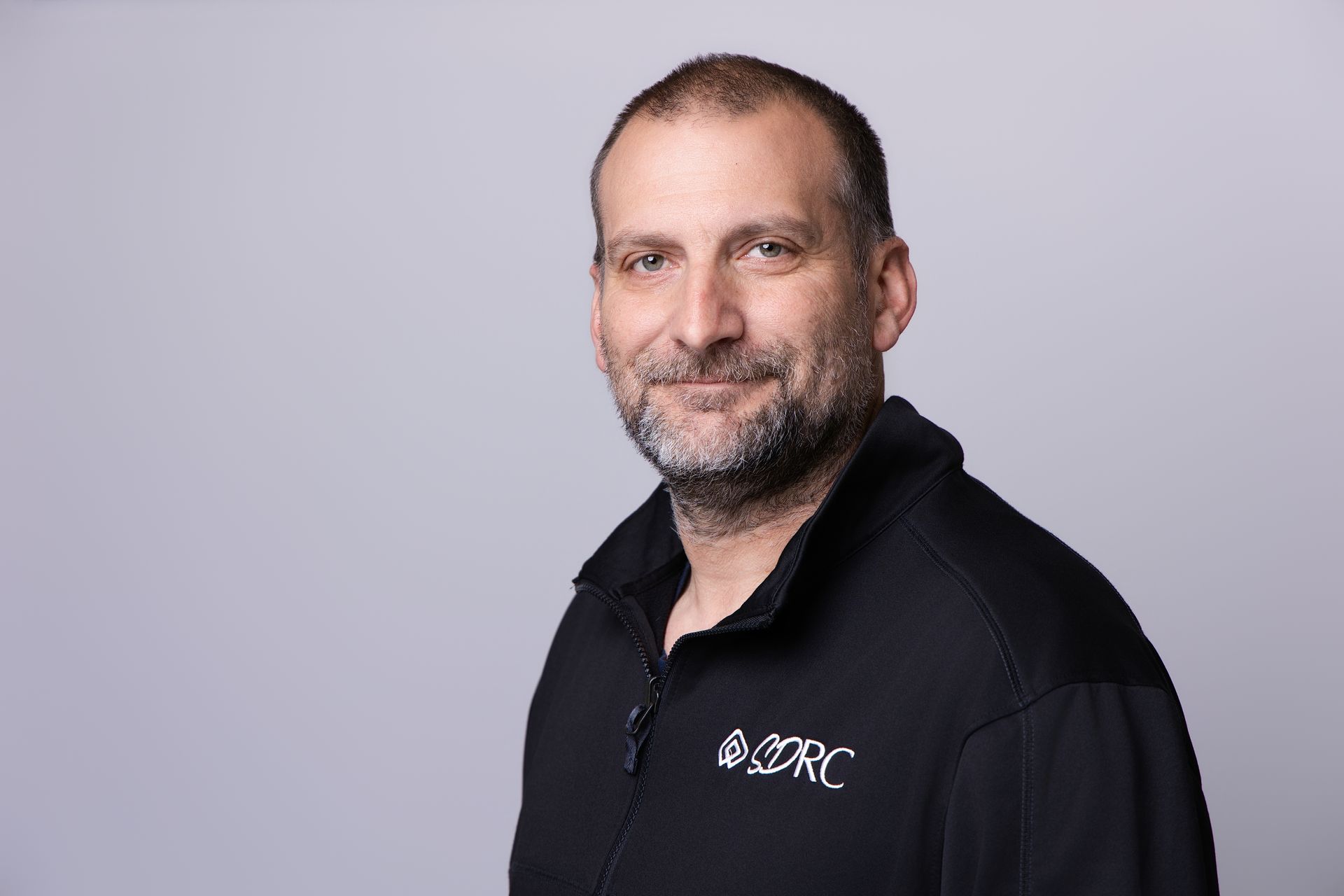 Smiling person in a black collared shirt against a light gray background