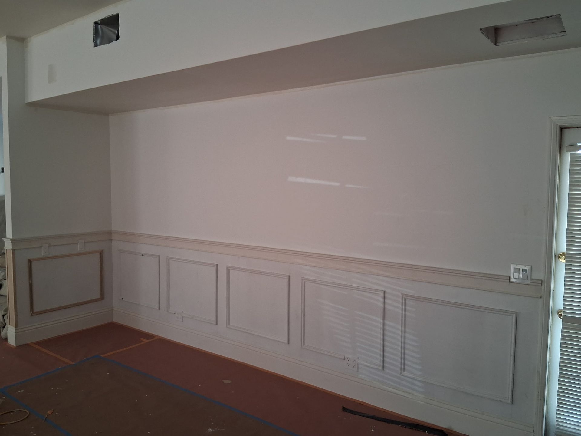 A room featuring cream-colored walls with decorative wainscoting and a dropped ceiling section.