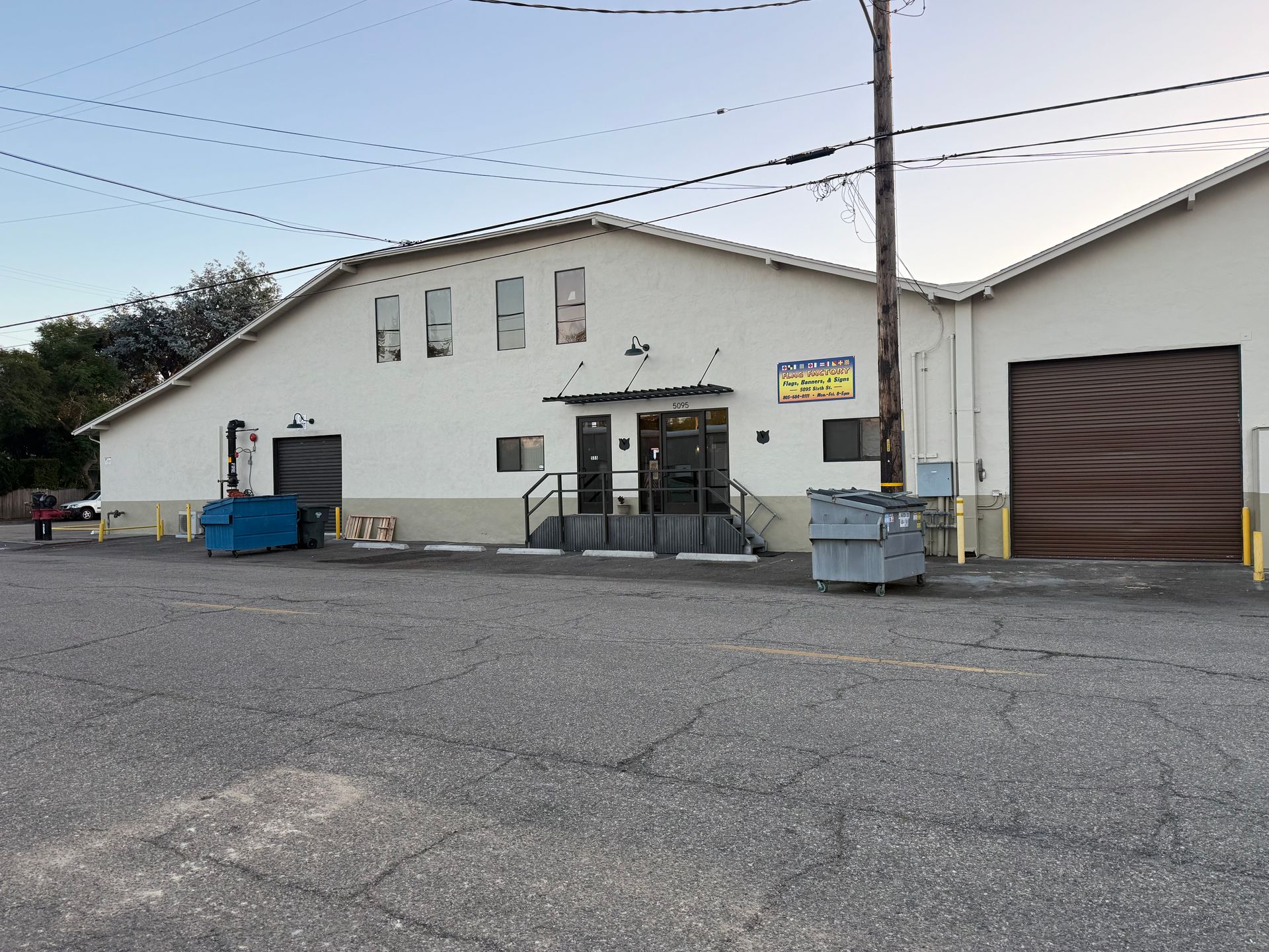 A light-colored, multi-section commercial building with large roll-up doors, an entrance with stairs, and a paved lot.