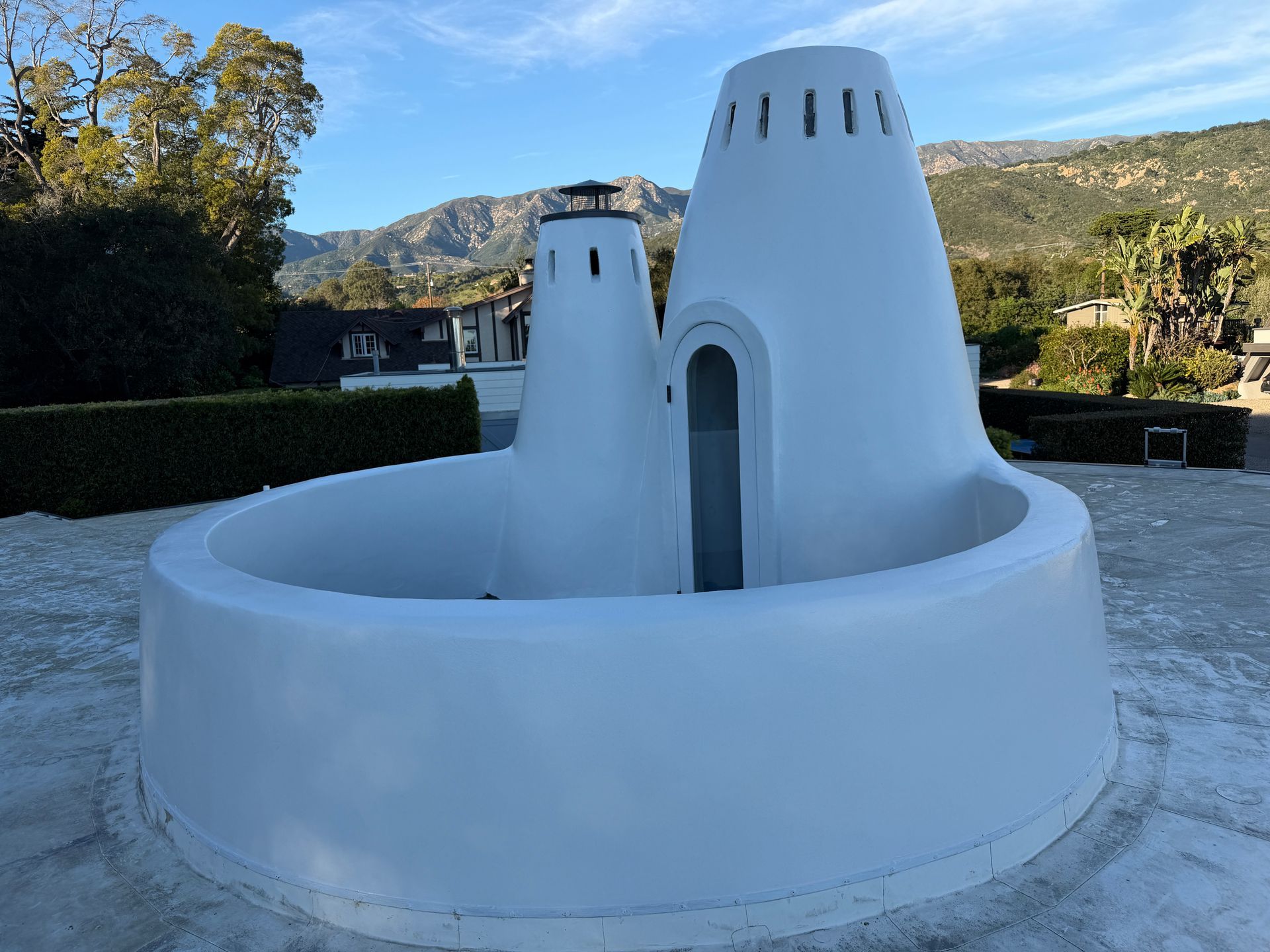 A white, cone-shaped outdoor sculpture or architectural structure with two tall towers stands on a stone patio.