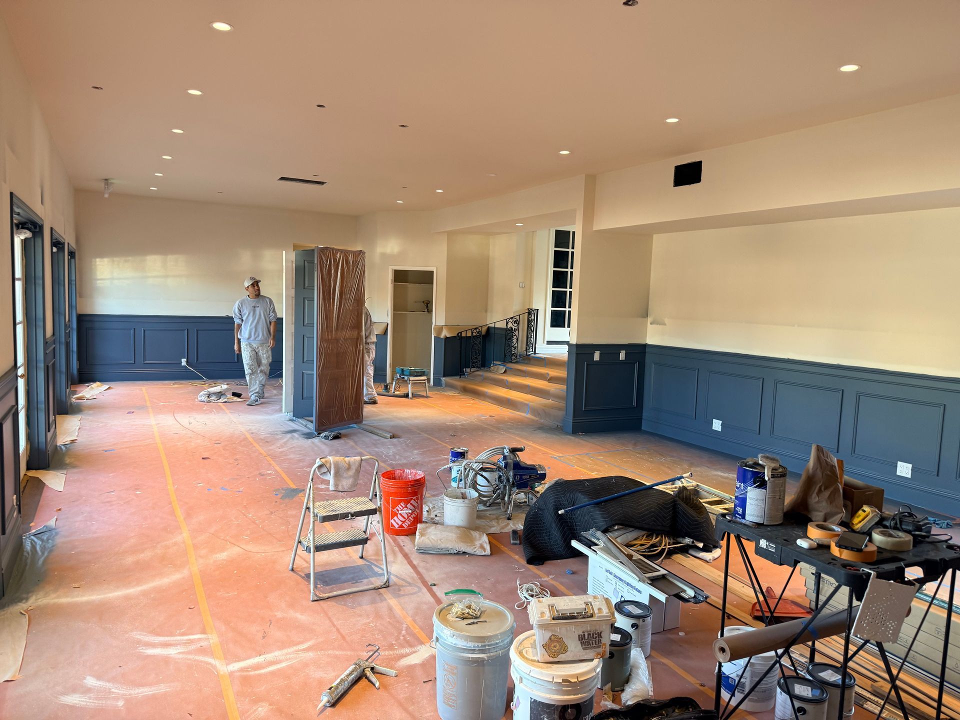 Interior room under construction with dark blue wainscoting, light walls, a worker, and scattered building supplies.
