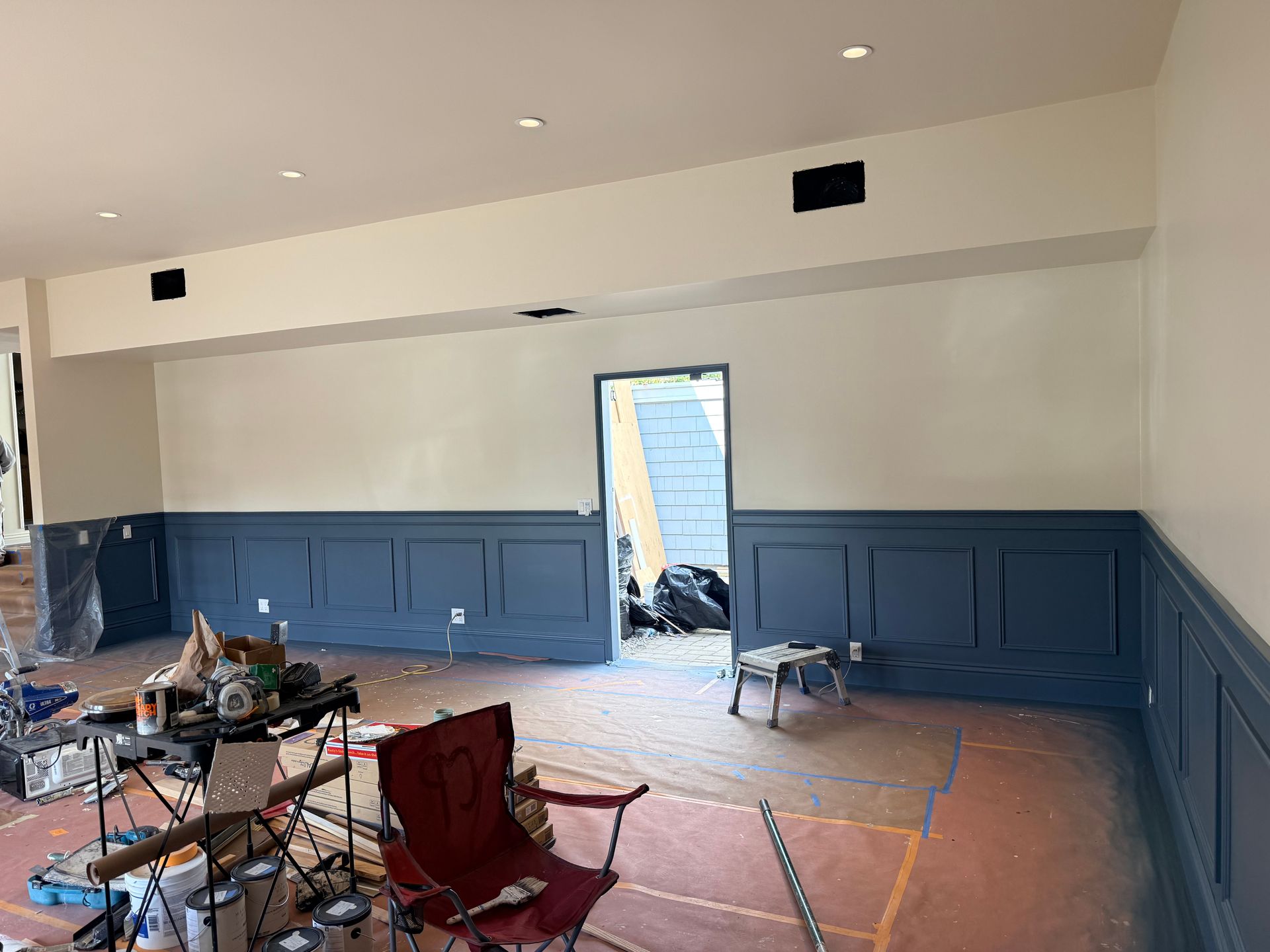 A room under renovation with dark blue wainscoting on the bottom half of the walls and off-white paint on the top half.