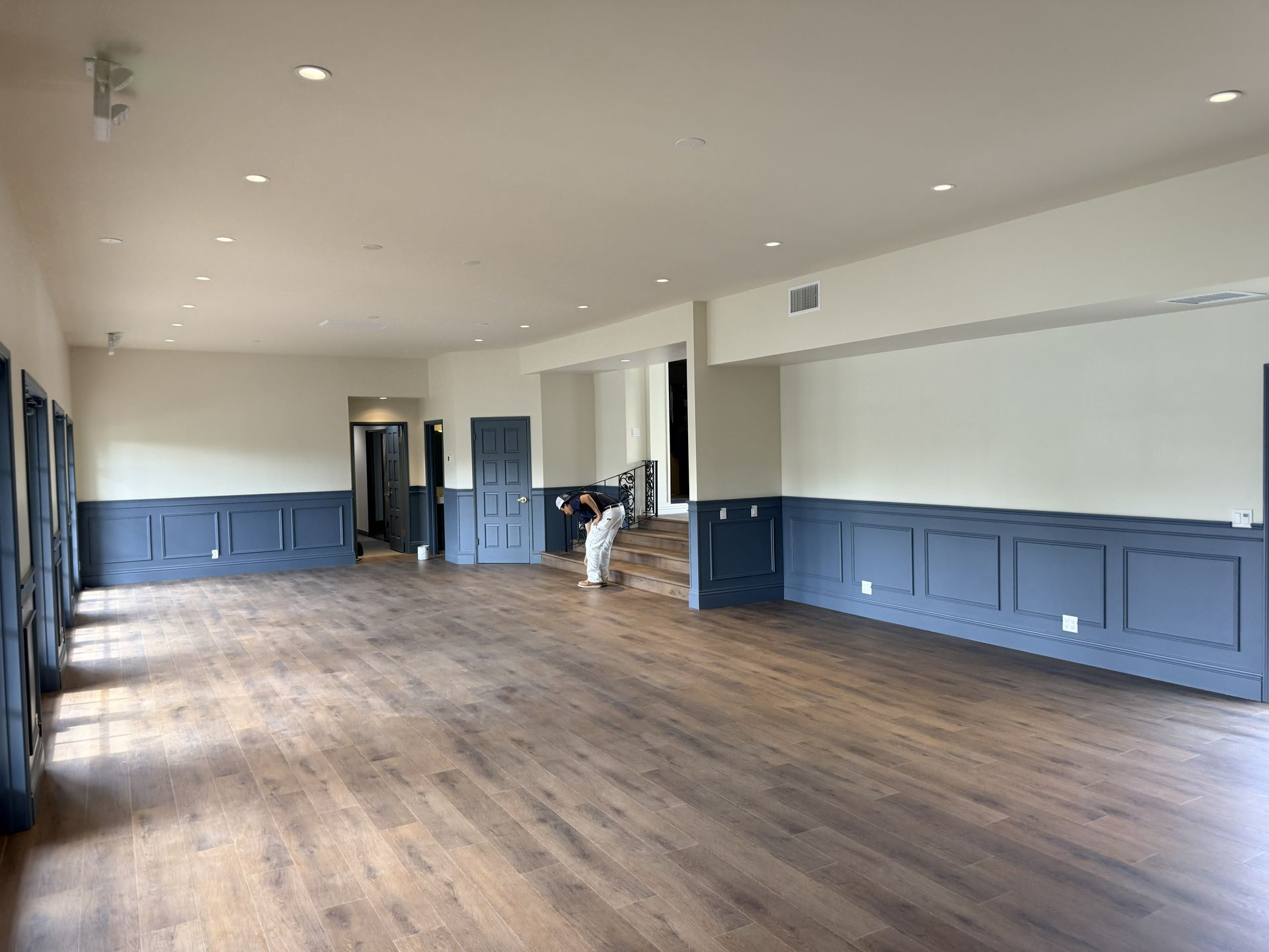 A bright, empty room with wood floors, cream upper walls, and dark blue paneled wainscoting.