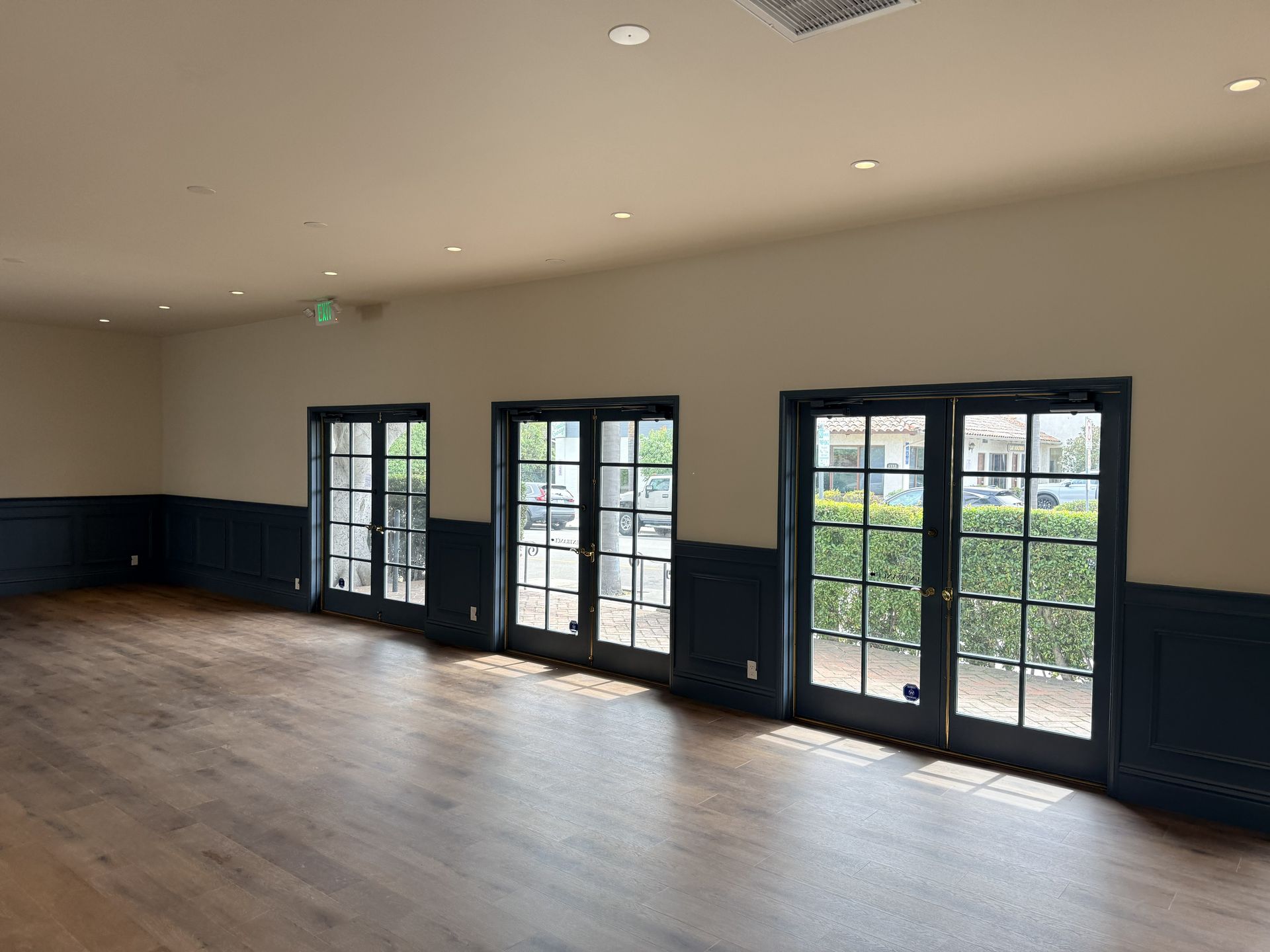 A spacious room with wood floors, cream walls, dark blue wainscoting, and three sets of glass doors leading outside.