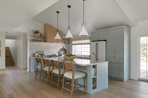 A modern kitchen with light blue cabinetry, a central island with four chairs, white marble accents, and pendant lighting.