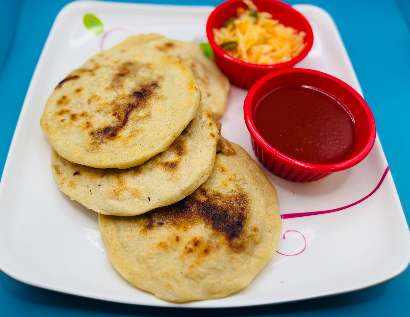 Plate of fried flatbreads with two small red bowls of chutney and grated cheese on a blue table