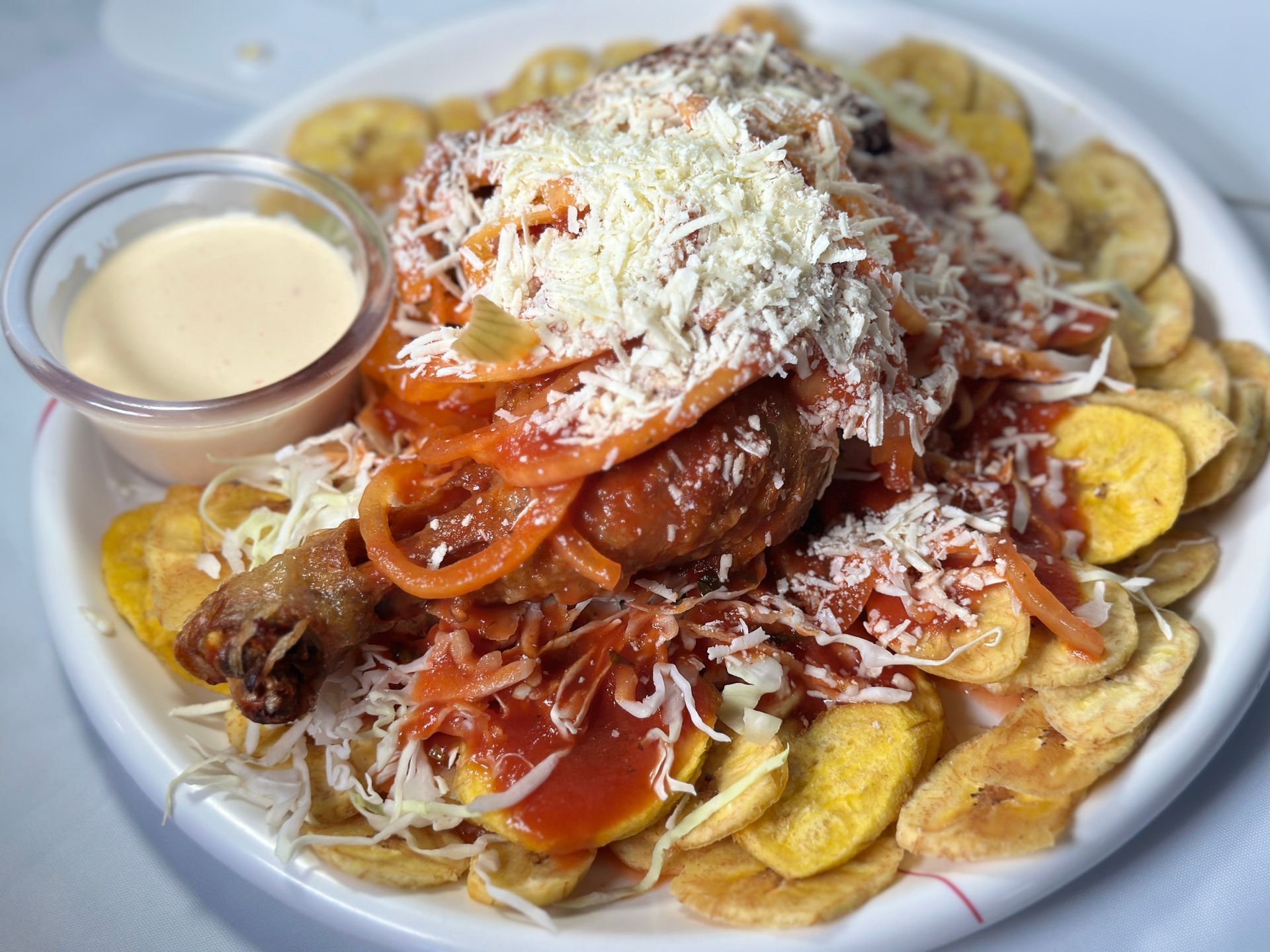 Plate of pasta topped with sauce and grated cheese, surrounded by plantain chips, with dipping sauce on the side