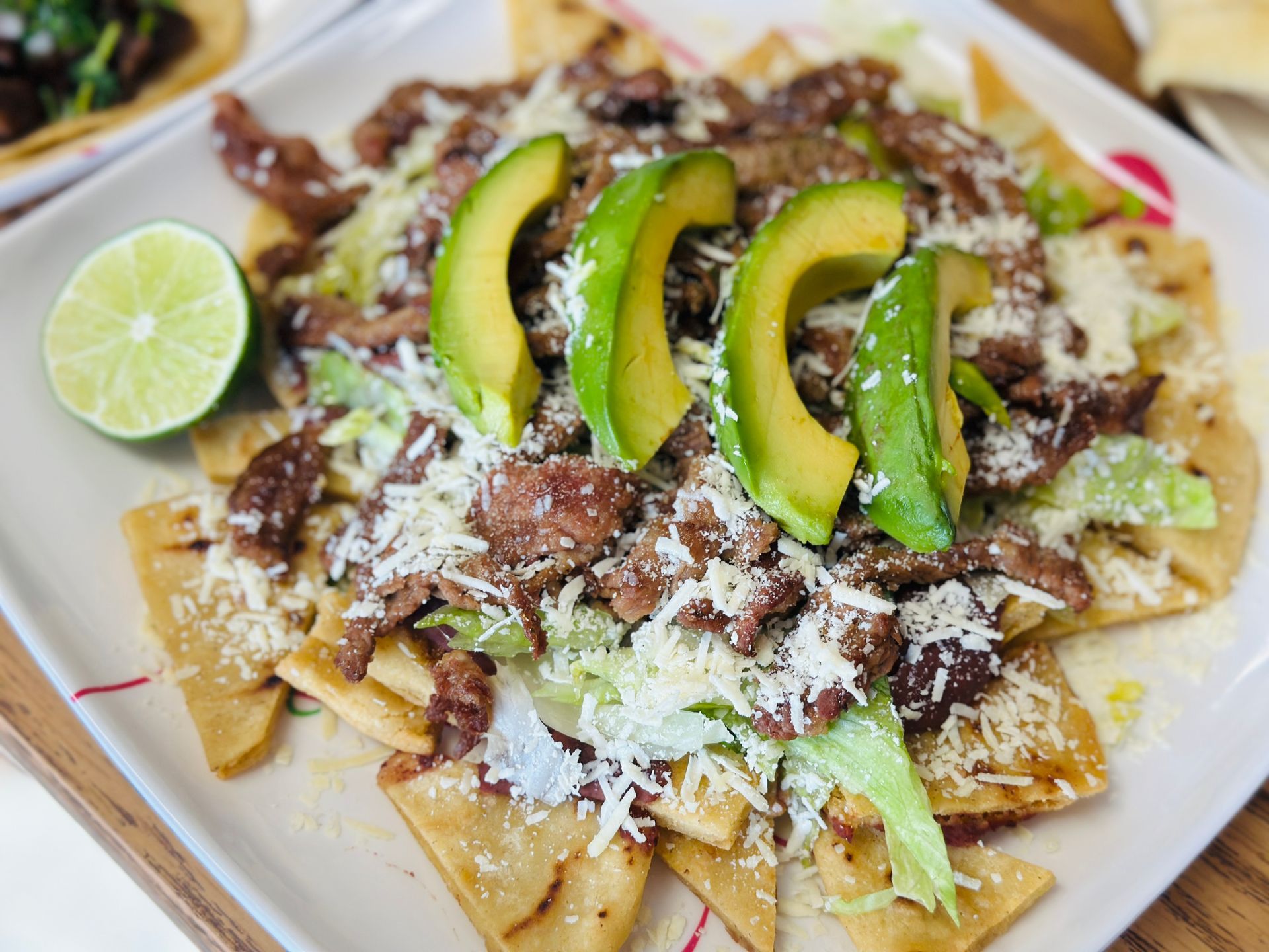 Loaded nachos topped with avocado slices, shredded cheese, and lime on a white plate