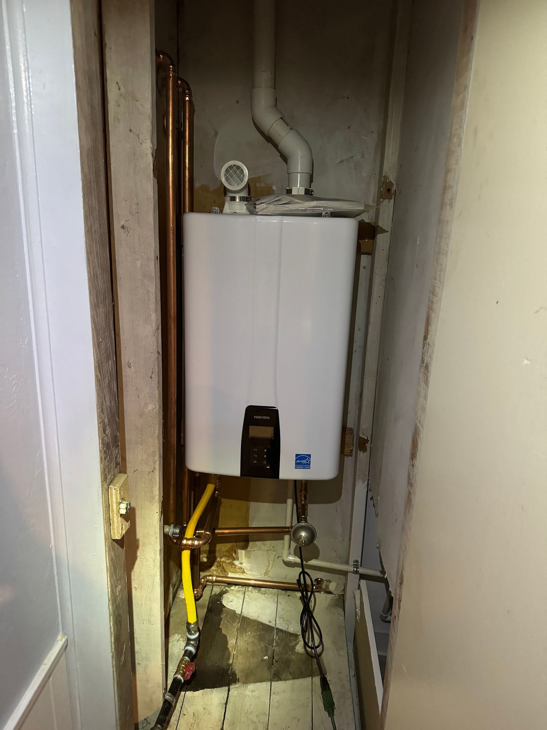 A white water heater is sitting in a narrow room next to a door.